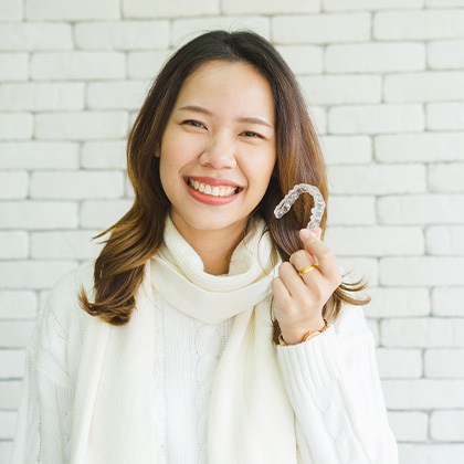 Woman in white sweater smiling holding Invisalign