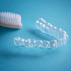 Clear aligners next to toothbrush on light blue surface