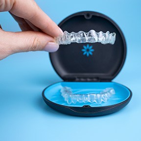 Fingers placing Invisalign into carrier case with light blue background