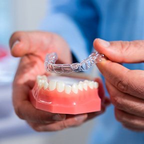 Dentist holding new Invisalign tray over model teeth