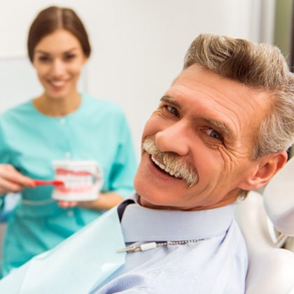 An older smiling man who’s just gotten dentures