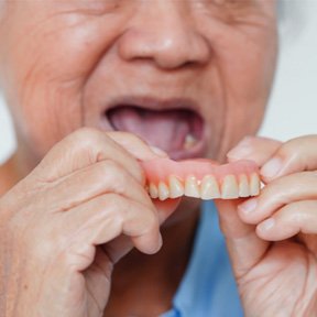 A woman removing a denture from her mouth