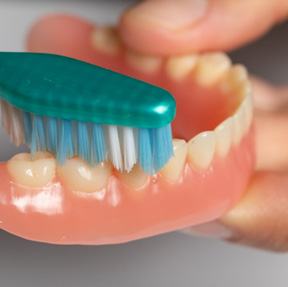 A toothbrush being used to clean a denture