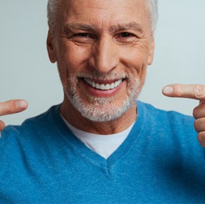 An older smiling man pointing to the dentures in his mouth