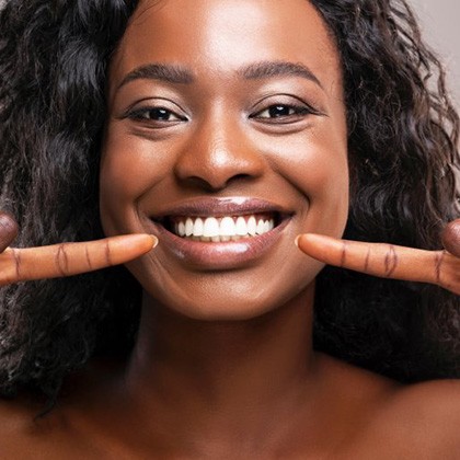 Woman pointing at her smile newly brightened with teeth whitening