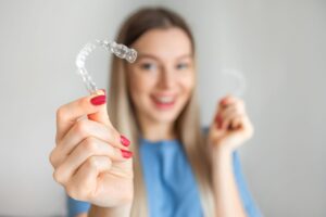 Woman with red nails blurry in the background holding Invisalign to foreground