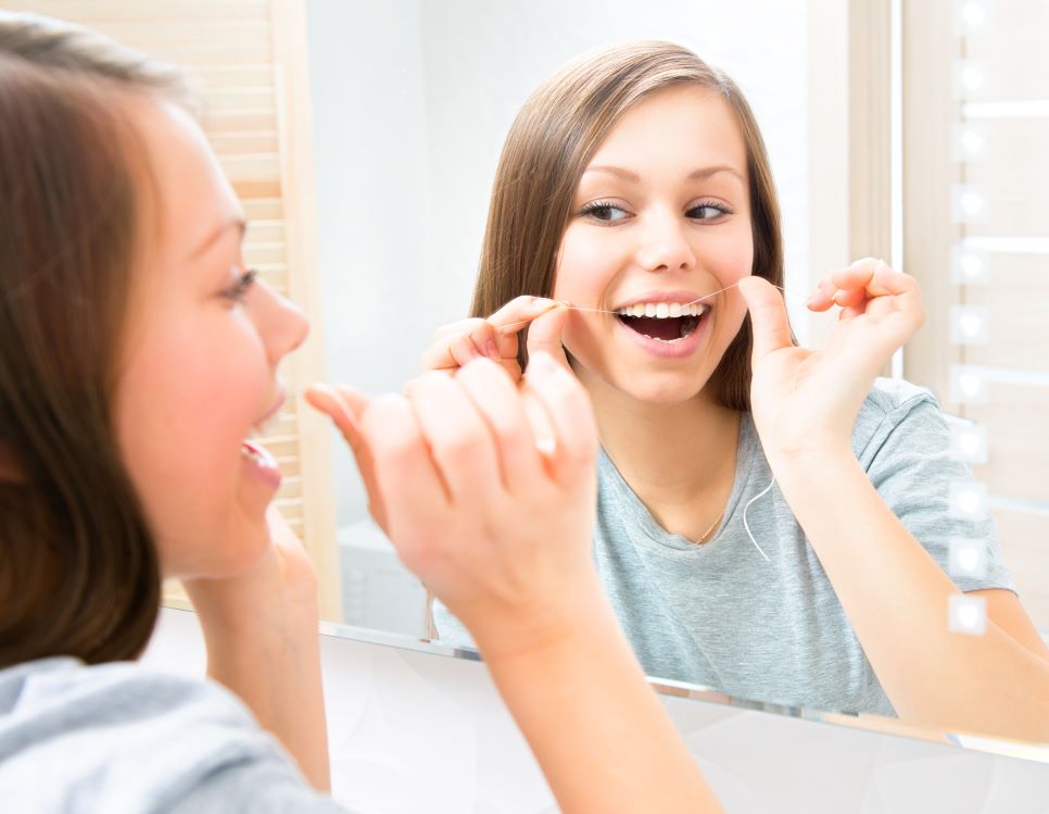 A woman flossing her teeth in the mirror.